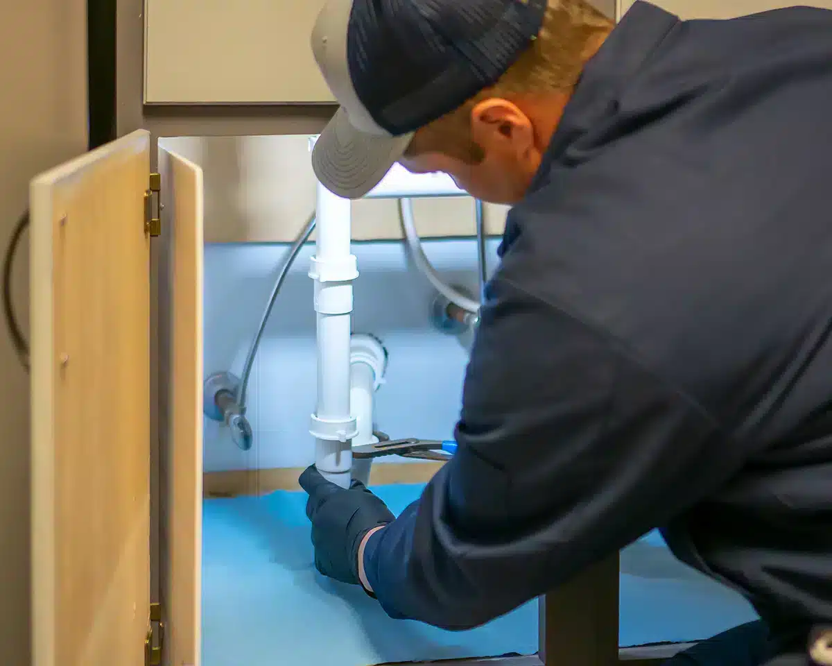 Plumber in Austell, GA working on pipes under a sink.